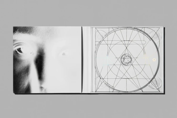 Monochromatic image of an opened CD case featuring a partial face on the left and a CD with geometric designs on the right.
