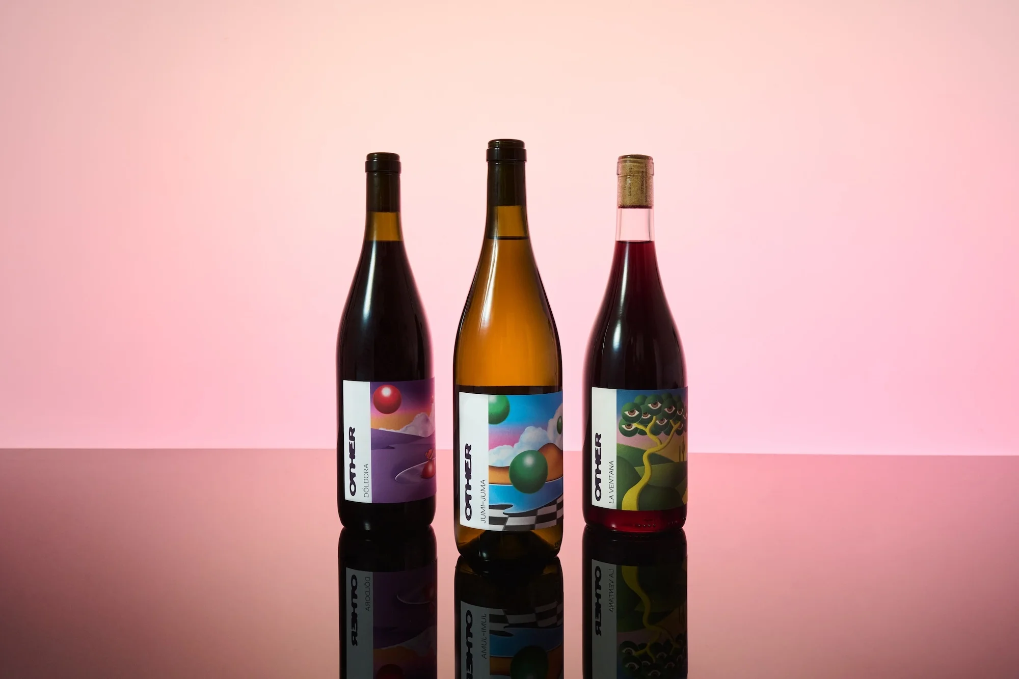 Three 'Other' wine bottles with colorful labels, displayed on a glossy surface with reflections, set against a gradient pink background.