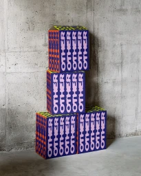 Stacked branded boxes with bold typographic print against a raw concrete wall and floor