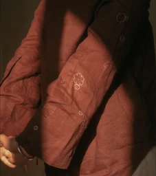 Close-up of a person wearing a rust red buttoned shirt with embroidered flower patterns and a dark outer garment