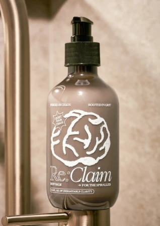 Pump bottle of Re:Claim body balm with a brain graphic, sitting next to a metal tap. Product shot, skincare, beauty.