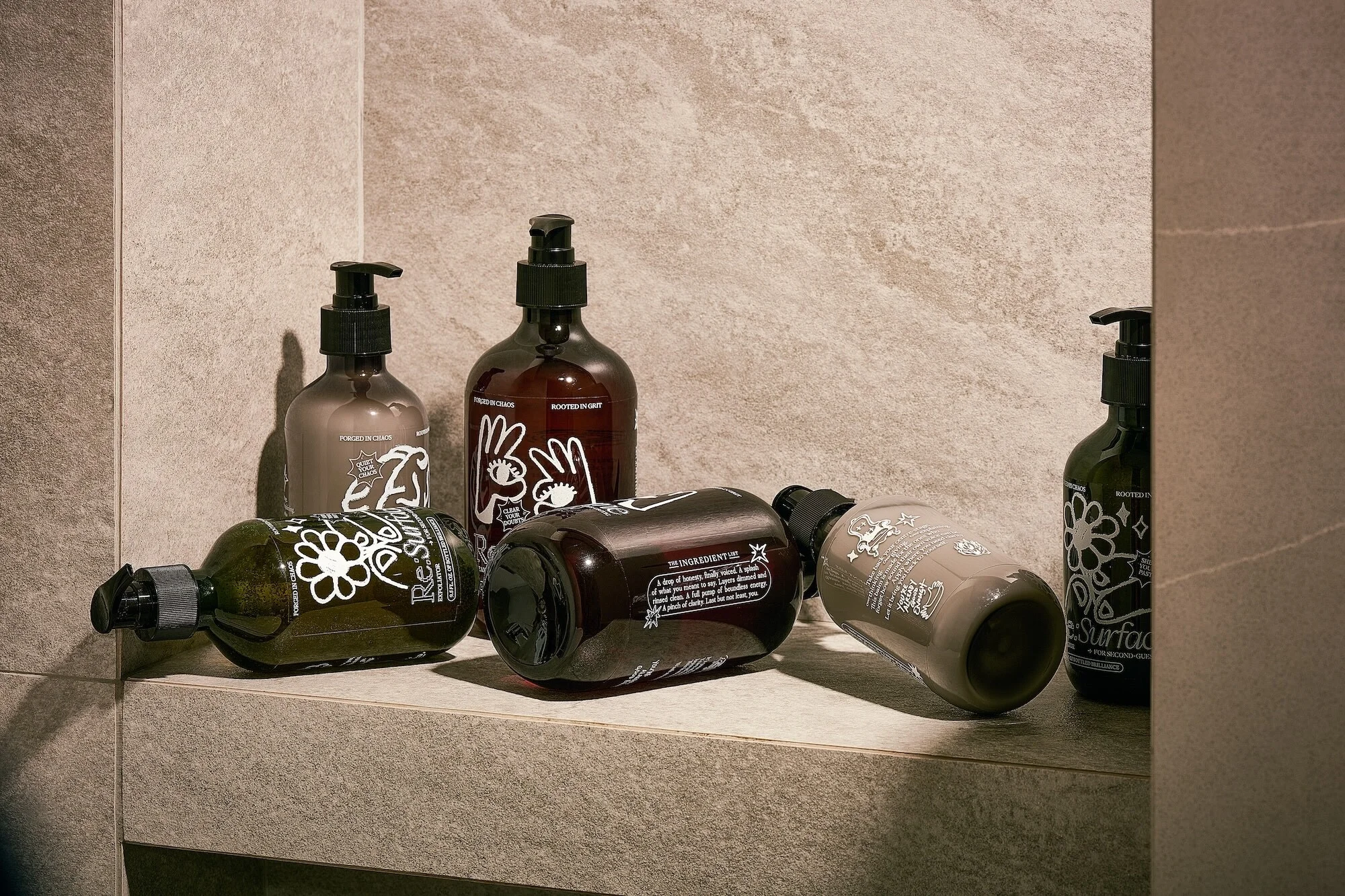 Collection of cosmetic bottles with pumps in varying shades of brown and green, neatly arranged on a tiled shelf against a tiled wall.