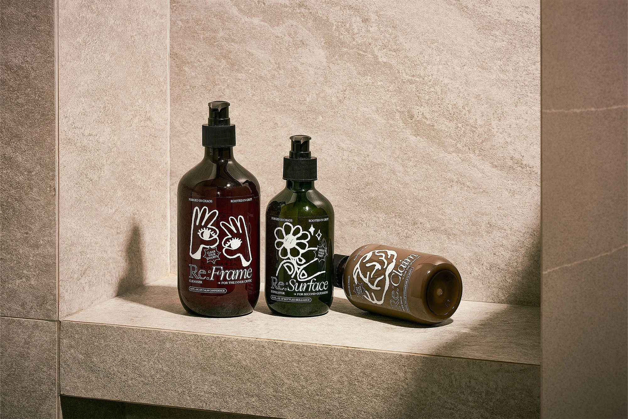 Three bottles of Re:Frame and Re:Surface shampoo and conditioner products on a grey stone shelf against a grey tile wall.
