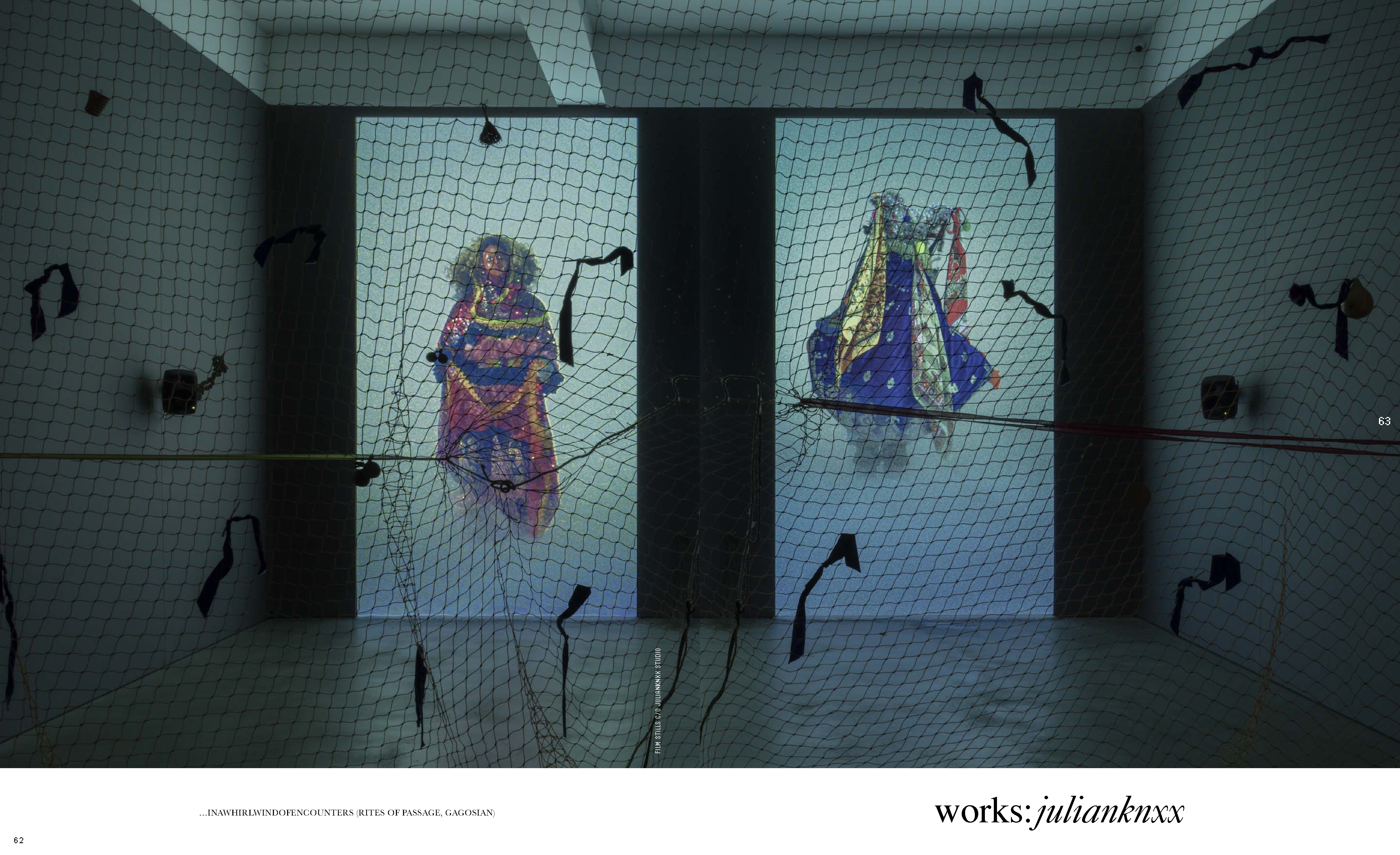 Art installation with two screens showing figures in ornate robes against a light blue background, viewed through a black netting.