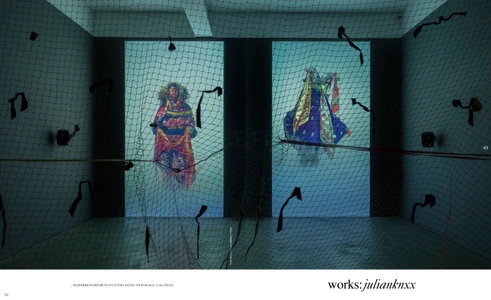 Installation view with a dark mesh net in foreground and two projected screens showing figures in colourful garments
