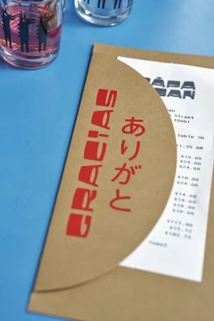 Receipt and paper sleeve on a blue surface next to glassware, featuring red printed text in English and Japanese.