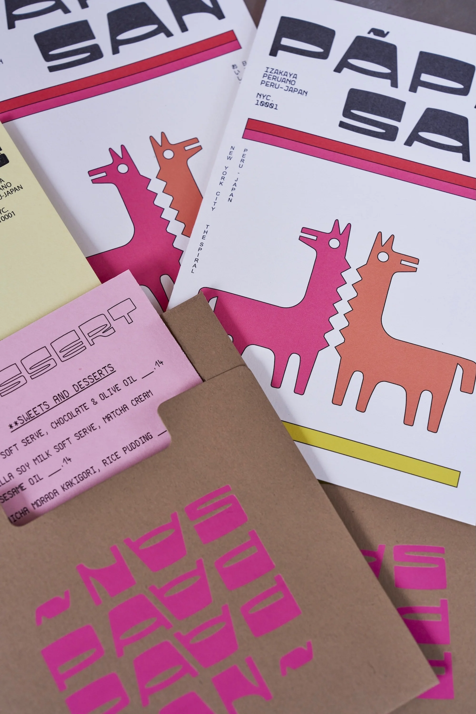 Several copies of a publication featuring llama illustrations in pink and orange, placed on a variety of colorful paper backgrounds.
