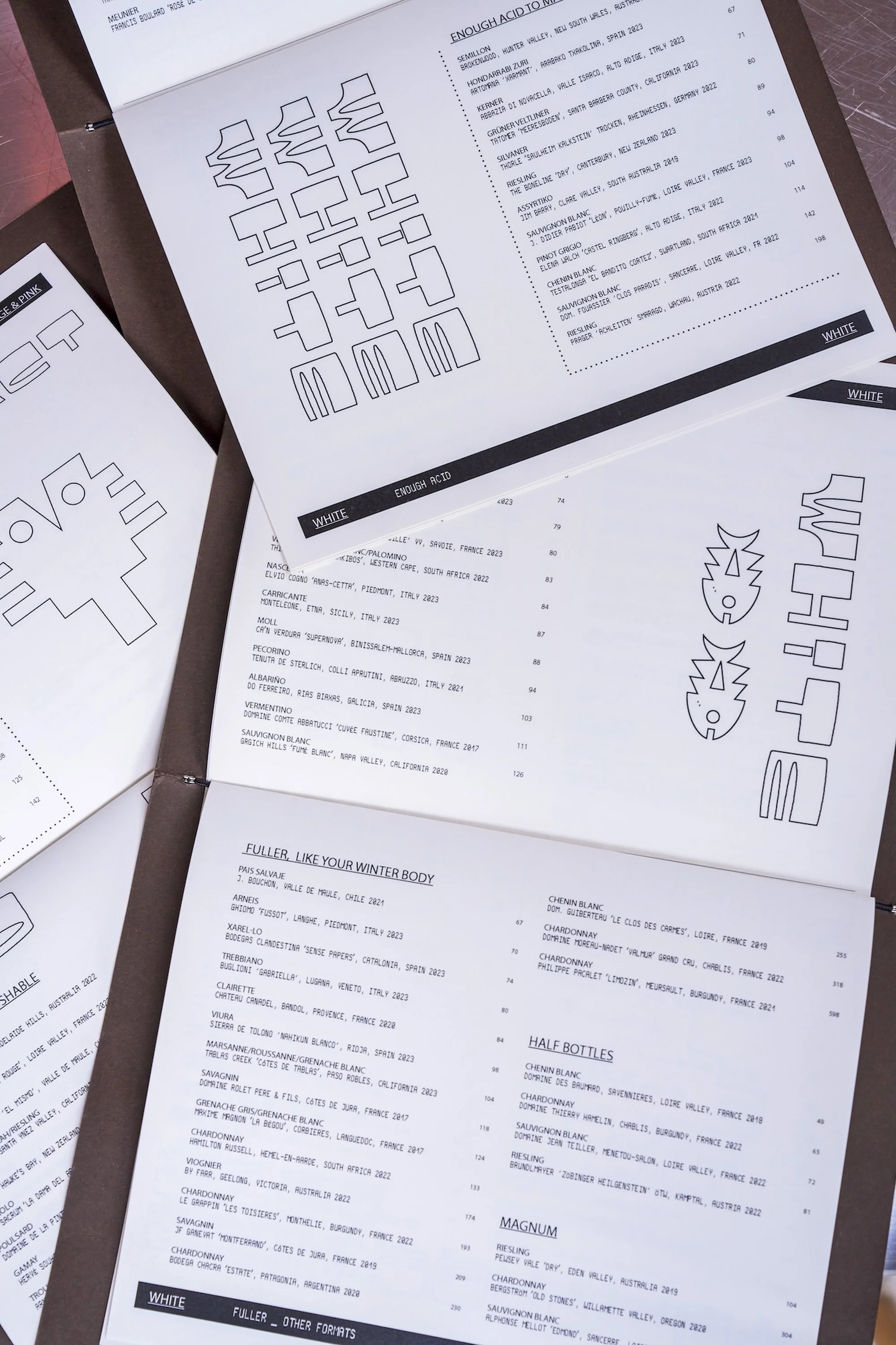 Close-up of open menus displaying organized lists of items and prices, featuring unique geometric artwork and bold typography.