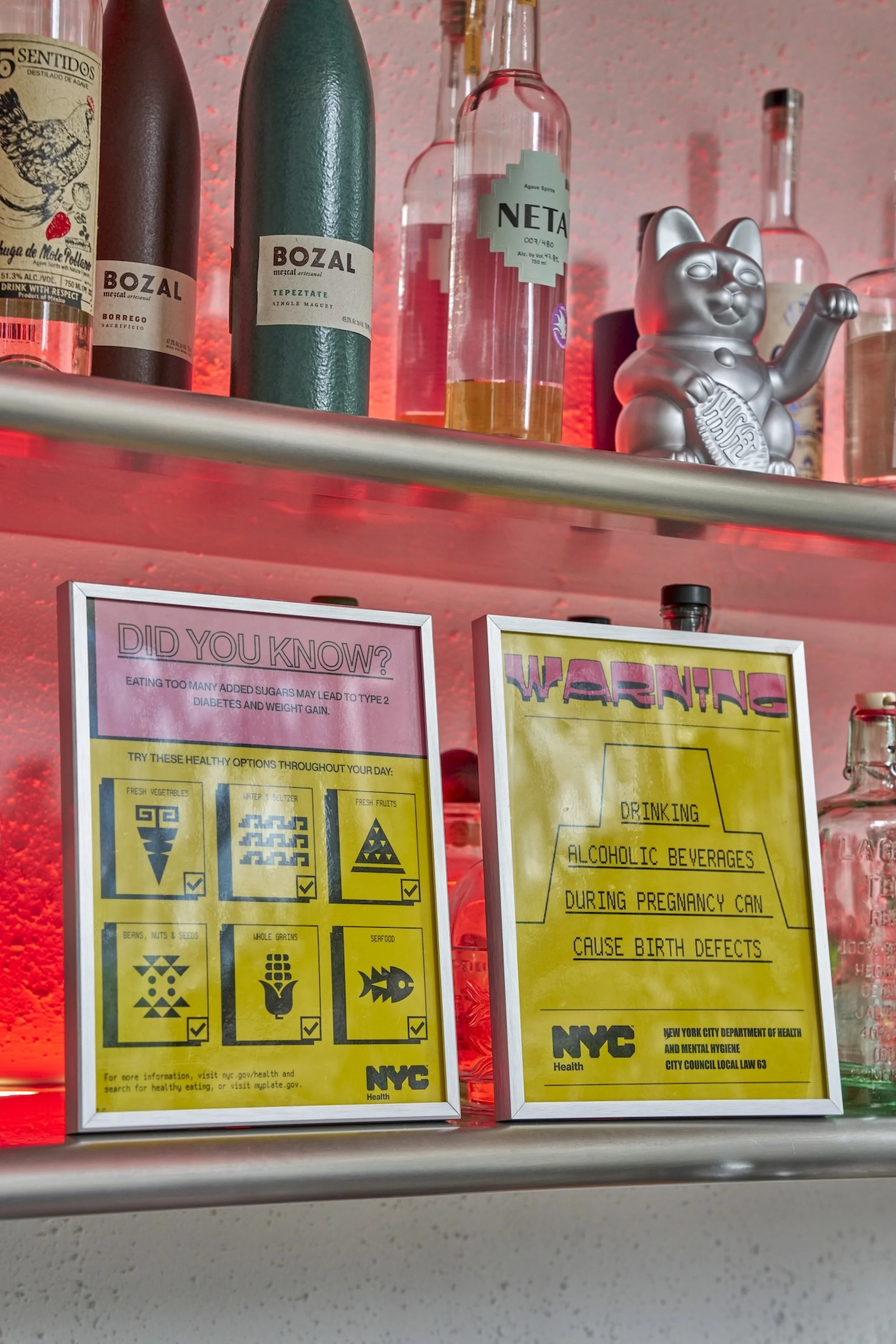 Bottles and signs on a shelf: liquor bottles including Bozal Mezcal, Neta Tequila, plus health warning signs about alcohol during pregnancy.
