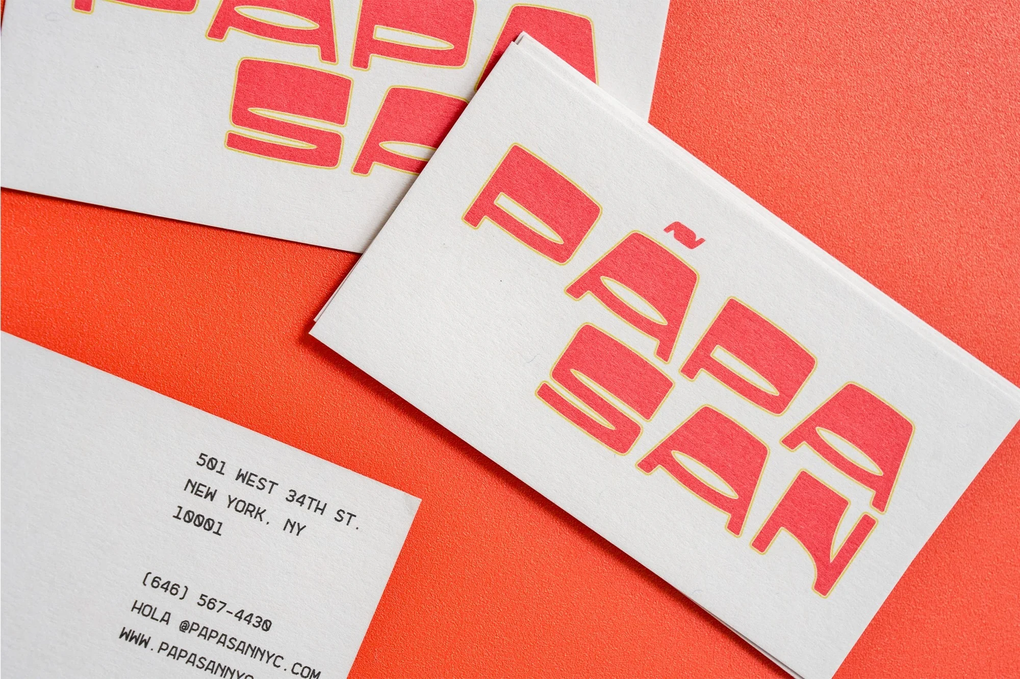 Close-up of stacked business cards on an orange background with the brand name and contact information printed on the cards.