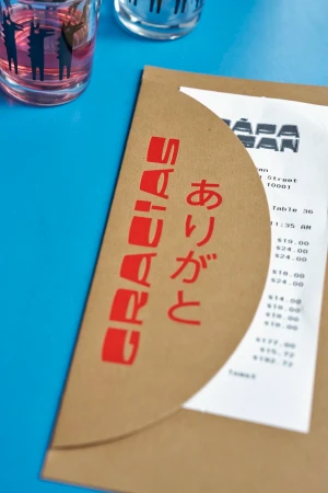 A brown paper envelope with red Japanese and English text next to a receipt and glasses on a bright blue surface