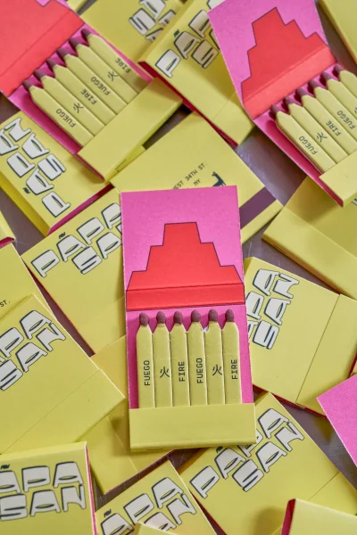 Top-down view of multiple yellow matchbooks with pink lids and printed typography arranged in a scattered composition.