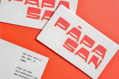 Stacked white business cards featuring the red Papa San logo placed on a vibrant orange textured paper background