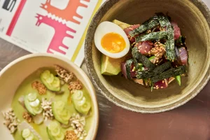 Two bowls of gourmet poke bowls with tuna, avocado, and soft-boiled egg next to a branded print menu for Papa San.