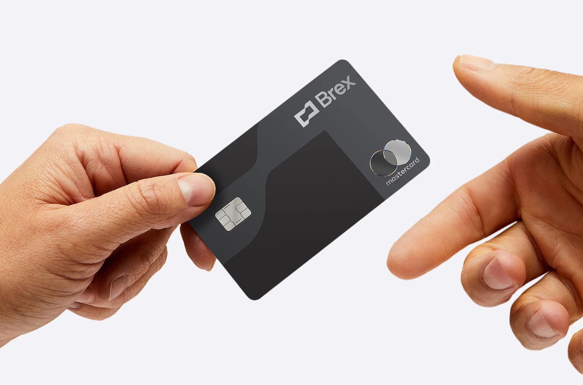 Person holds a gray Brex Mastercard in front of a white background. The card has a logo, chip, and Mastercard symbol.