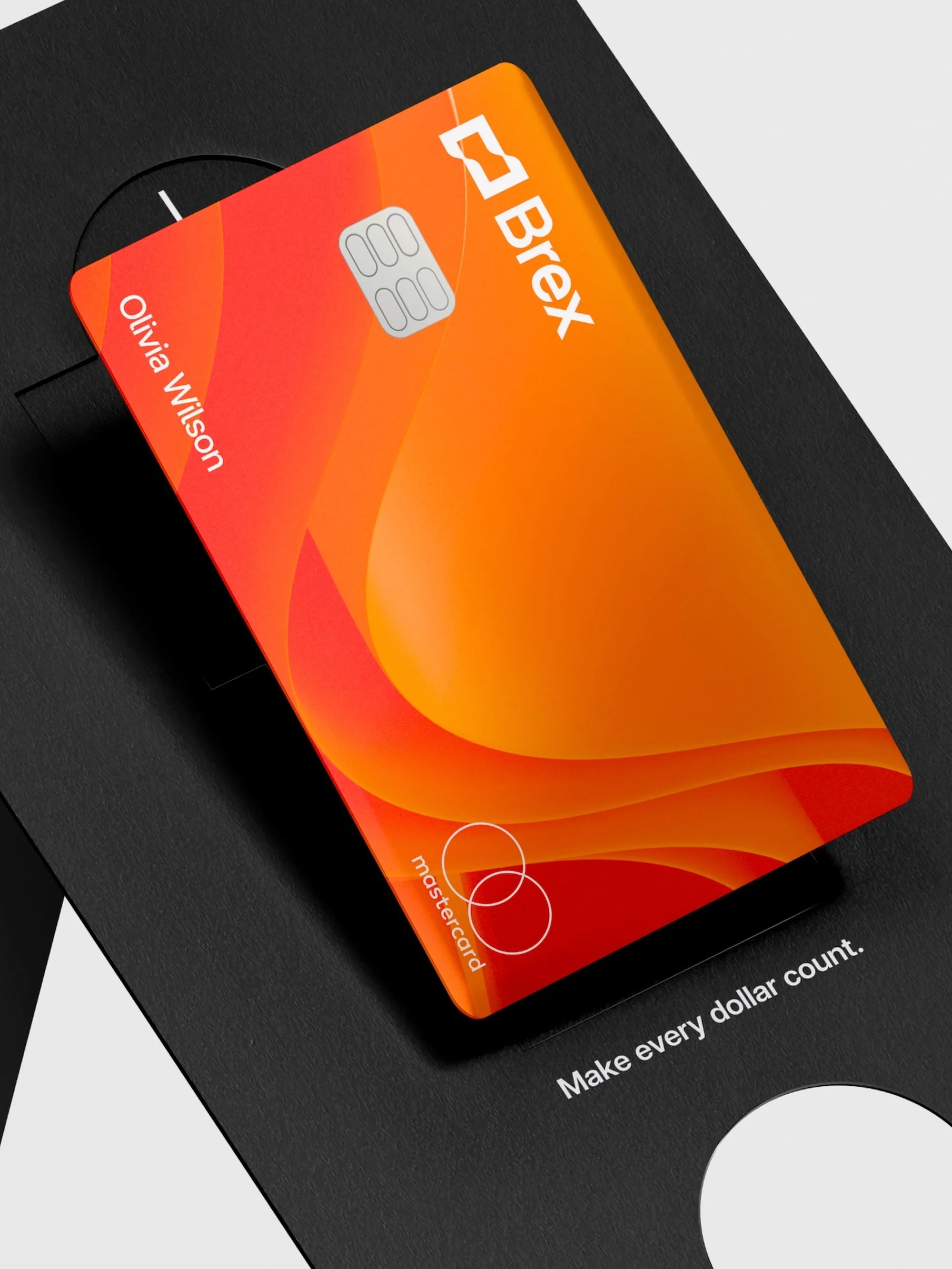 Close-up of an orange Brex Mastercard credit card on a black branded card holder with the text 'Make every dollar count'.