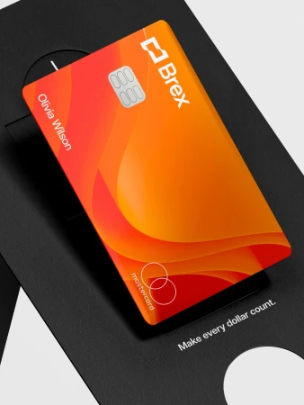 Close-up of an orange Brex Mastercard credit card on a black branded card holder with the text 'Make every dollar count'.