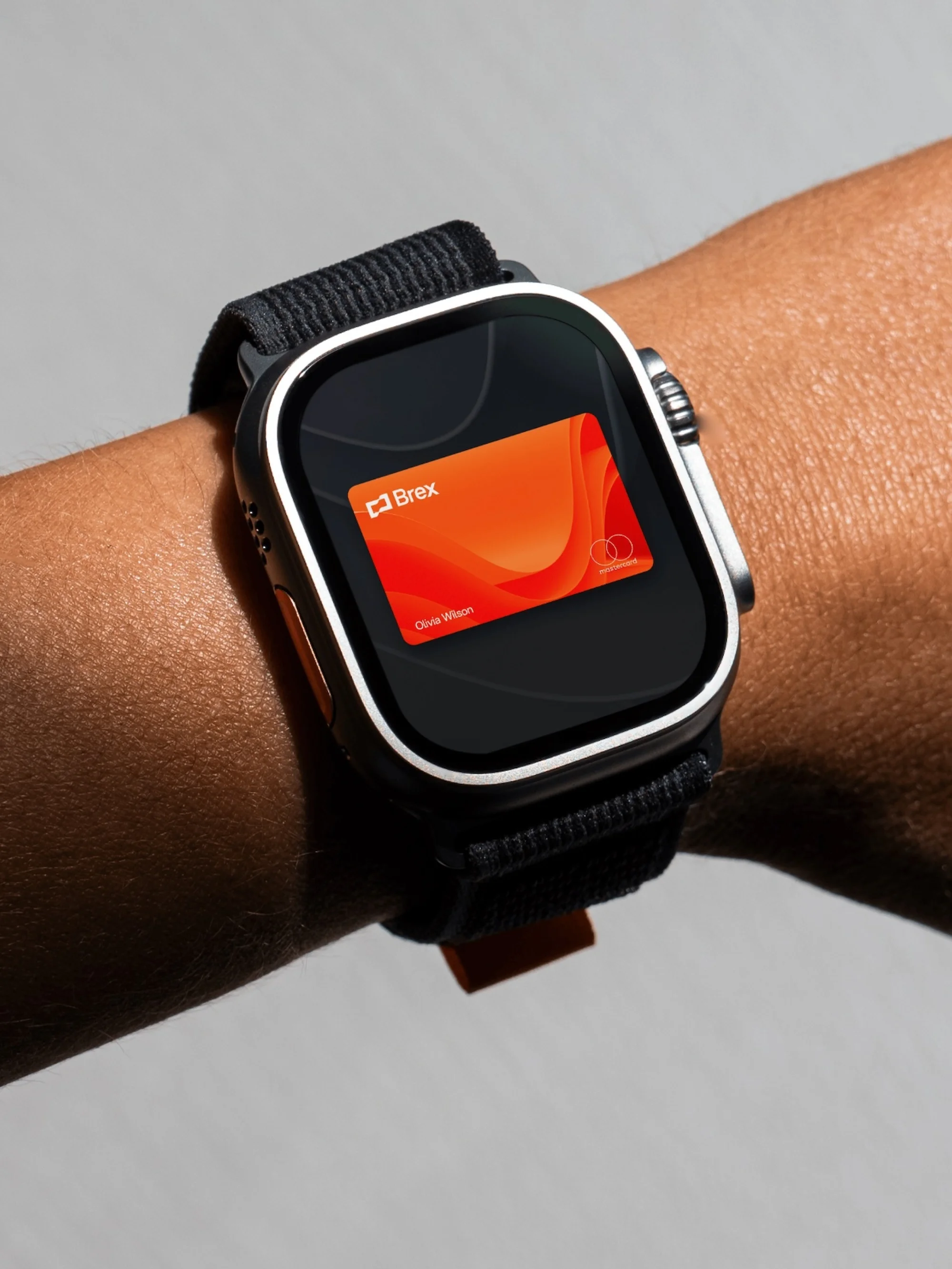 Close-up of a wrist wearing a smart watch displaying a digital card, set against a neutral grey background. Wrist watch has a black band.