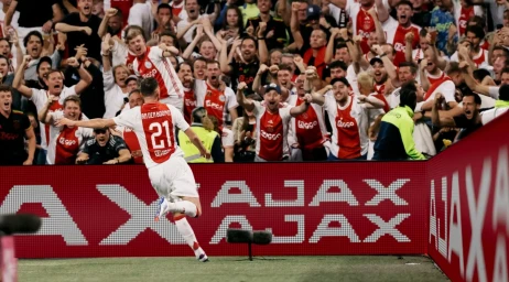 Ajax soccer player celebrating in front of a cheering crowd and digital advertising boards displaying the brand name