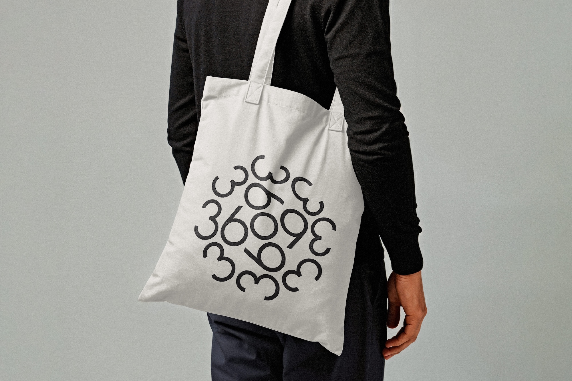 Person wearing a long-sleeve shirt and carrying a white tote bag featuring black numbers arranged in a circular pattern.