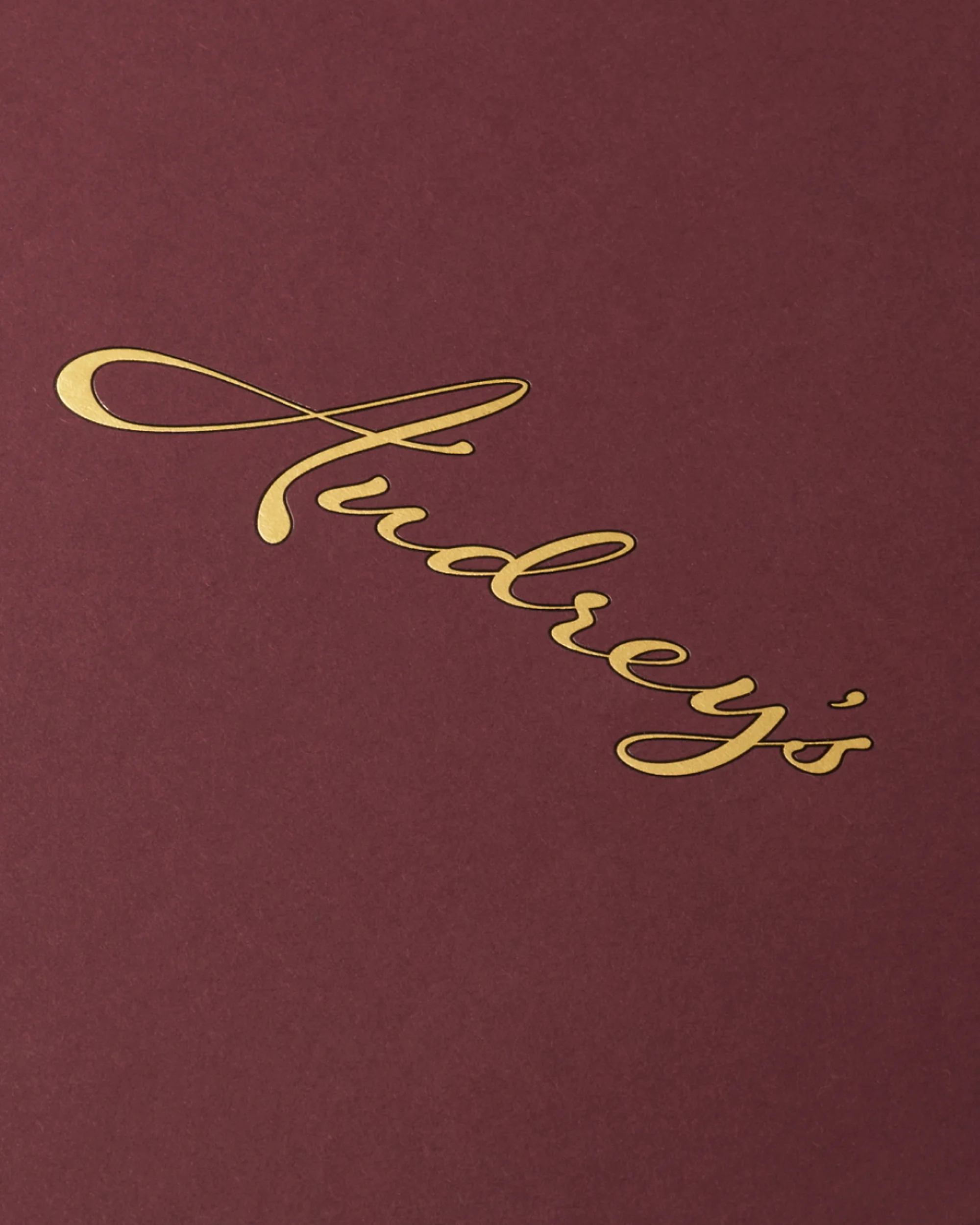 Elegant close-up of the golden script 'Audrey's' on a deep red surface, creating a sophisticated and luxurious visual appeal.