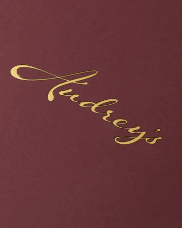 Elegant close-up of the golden script 'Audrey's' on a deep red surface, creating a sophisticated and luxurious visual appeal.