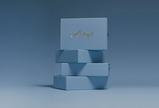 A stack of four light blue rectangular chocolate boxes with gold script branding against a minimalist blue studio backdrop.