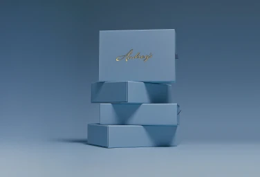 A stack of four light blue rectangular chocolate boxes with gold script branding against a minimalist blue studio backdrop.
