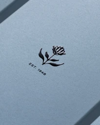 Embossed dark silver flower illustration and est 1948 text on light blue textured paper packaging surface.