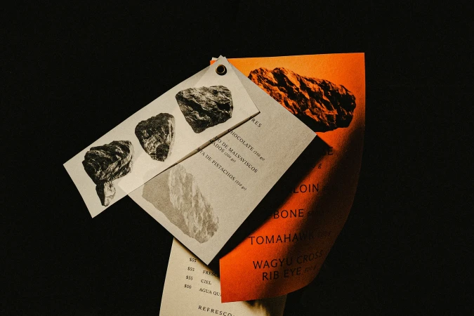 Close-up of offset printed restaurant menus featuring food images, prices, and text on warm-toned paper in a dark setting.