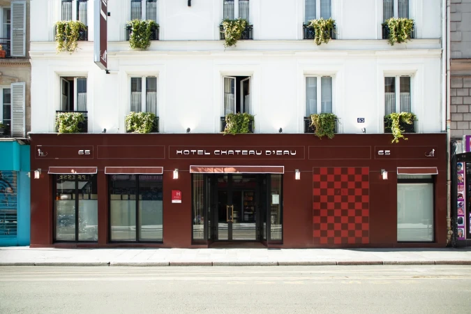 Exterior of Hotel Chateau D'eau in Paris featuring a brown facade with a checkered pattern, multiple windows, and green plants.