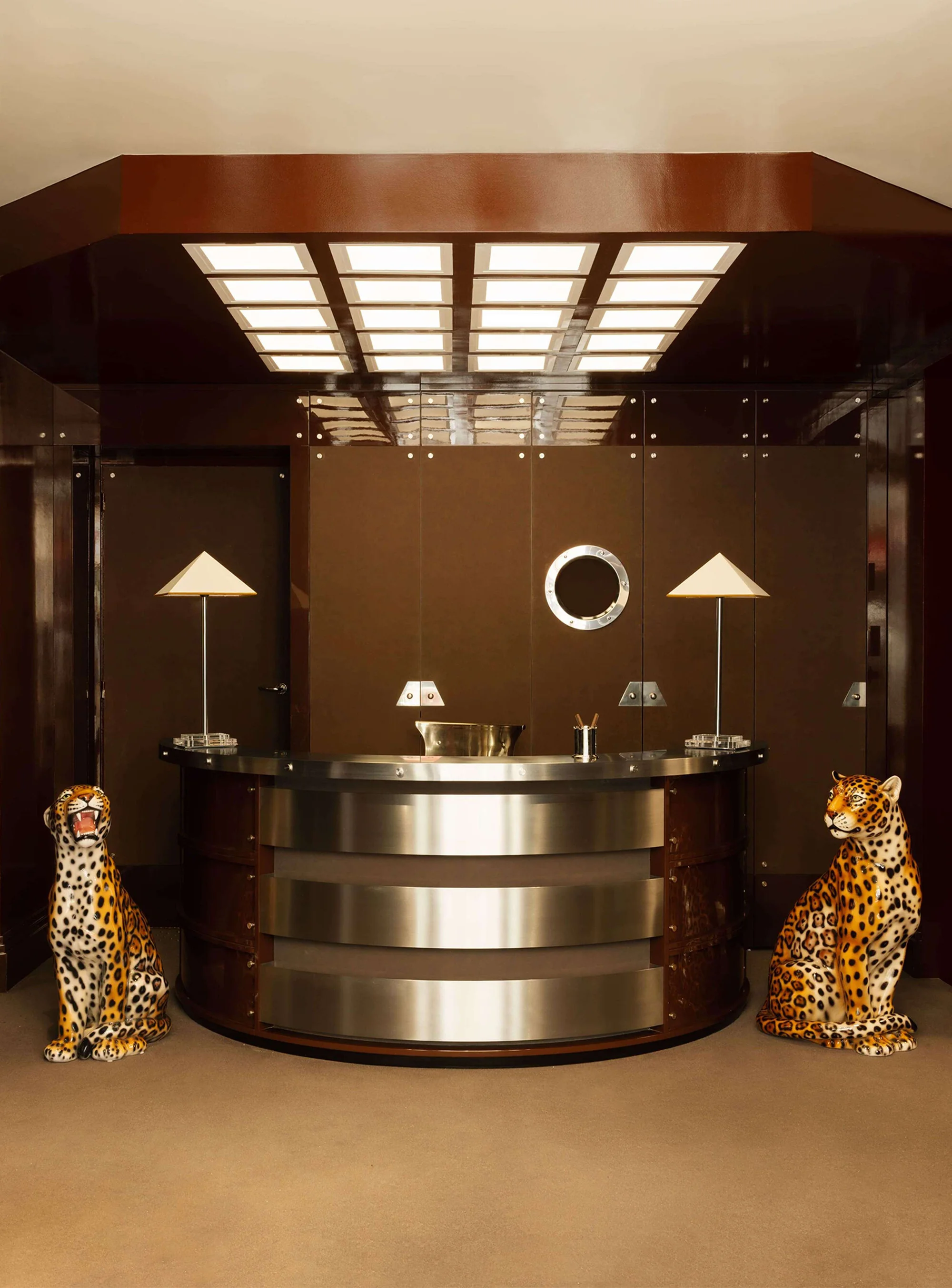 Reception area featuring a semicircular desk with two lamps, flanked by matching ceramic jaguar statues against a brown paneled backdrop.