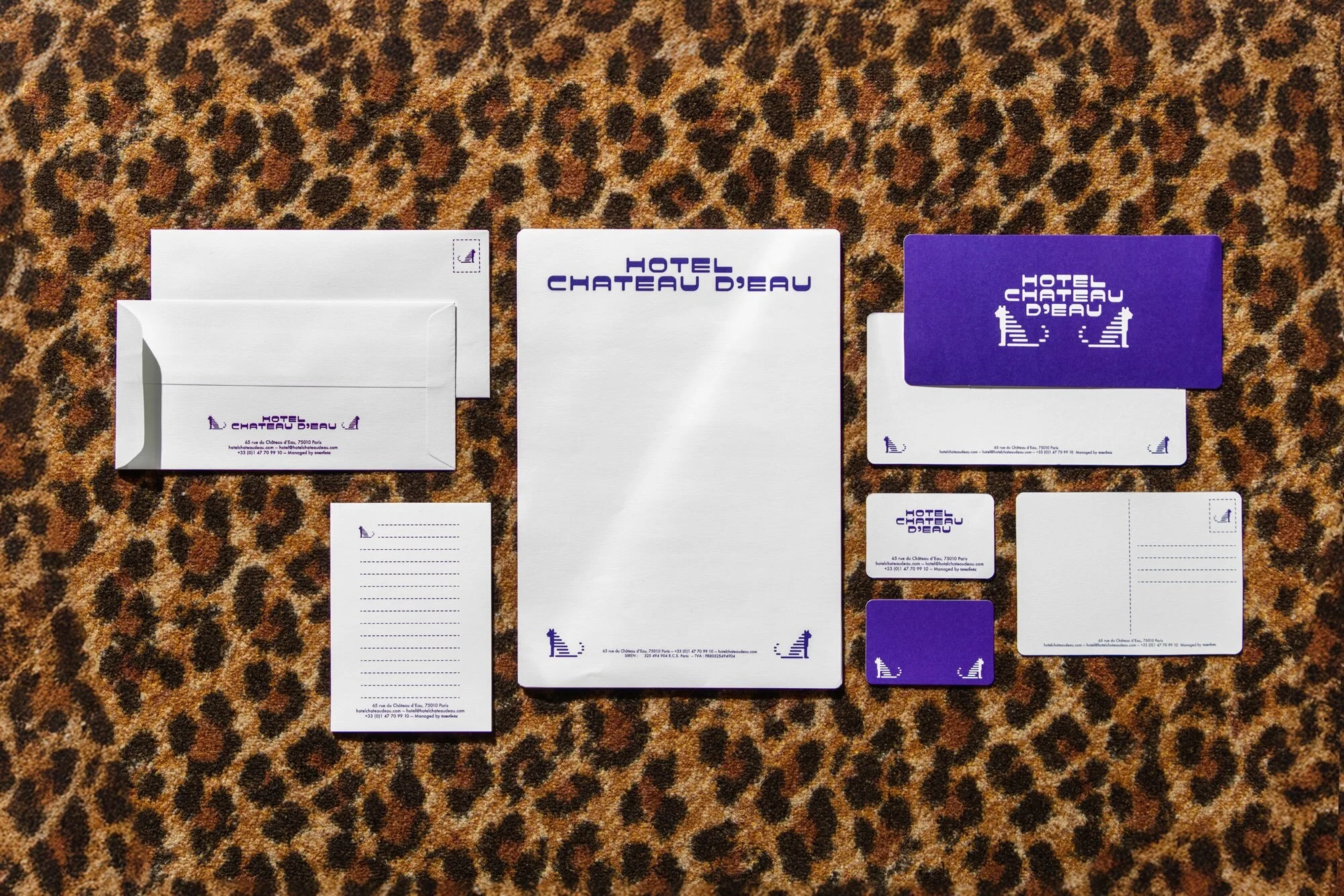 Hotel stationary, including letterhead, envelopes, and a postcard, are arranged on a brown and black leopard print surface.