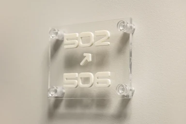 Clear acrylic room number sign mounted on a neutral wall displaying numbers 502 and 506 with an upward arrow for Hôtel Château d'Eau.