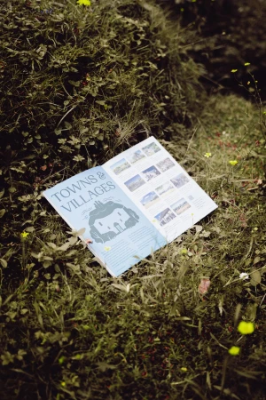 An open booklet titled Towns and Villages rests on green moss and grass outdoors.
