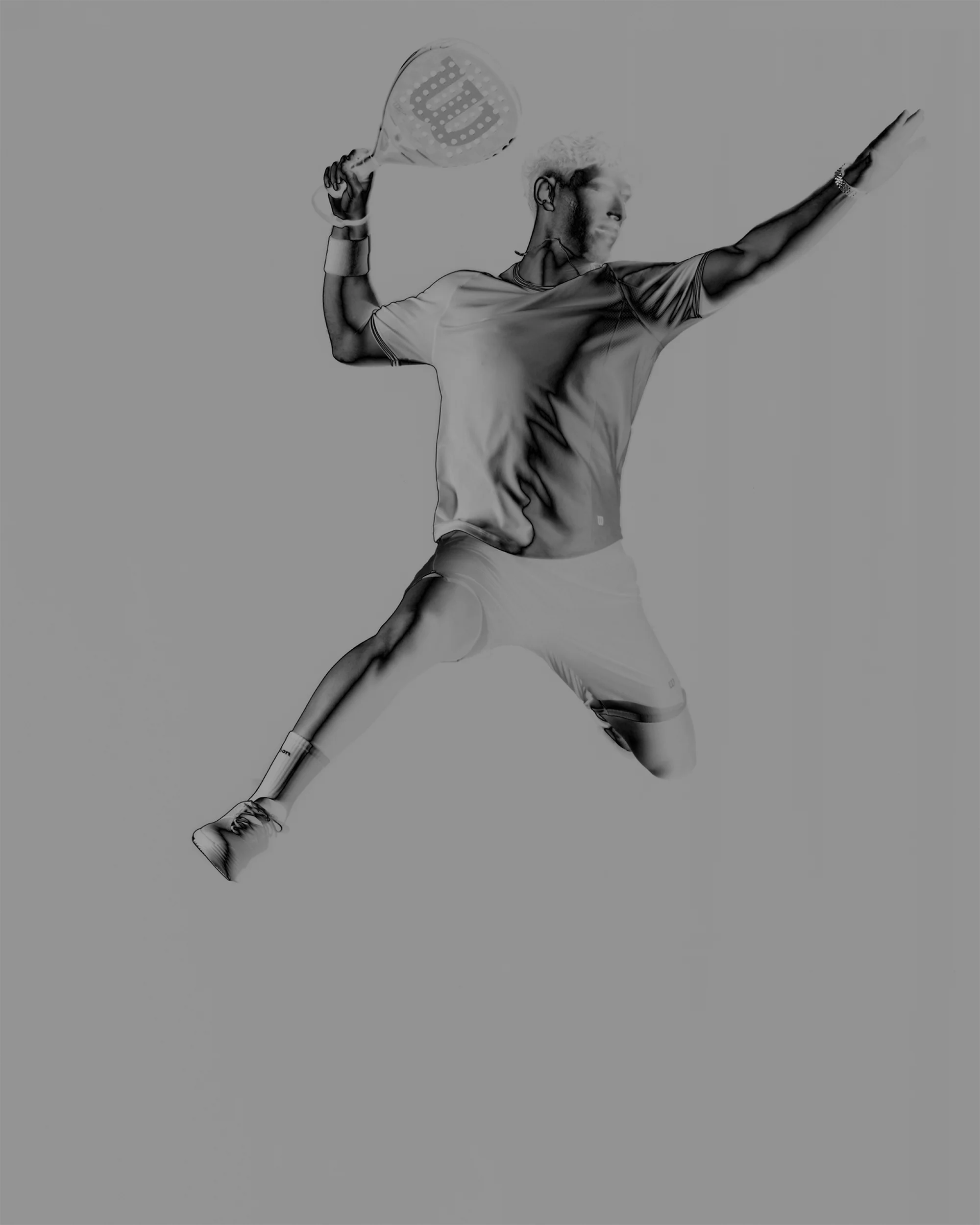 Action shot of a man in mid-air swinging a padel racket with outstretched arm and legs, set against a plain gray background.