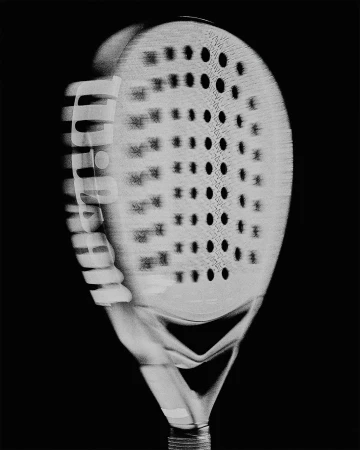 Monochrome image of padel racket against black background, showing the perforated surface and handle grip in a studio setting.