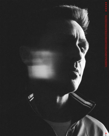 Monochrome portrait of a man in a track jacket with motion blur over his face against a dark background with red dots on the right.