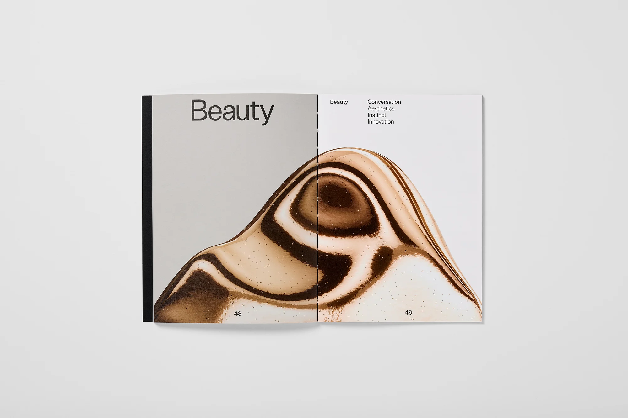 Open magazine featuring a sculptural wave form with beige and brown swirls on right page and 'Beauty' typography on the left page.