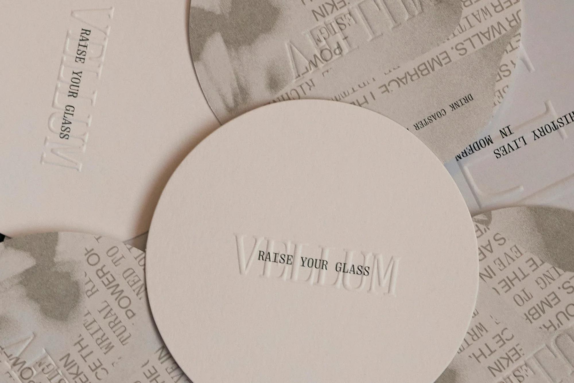 Close-up of stacked round coasters with embossed text reading 'Raise Your Glass,' featuring a minimalist design with a focus on texture.