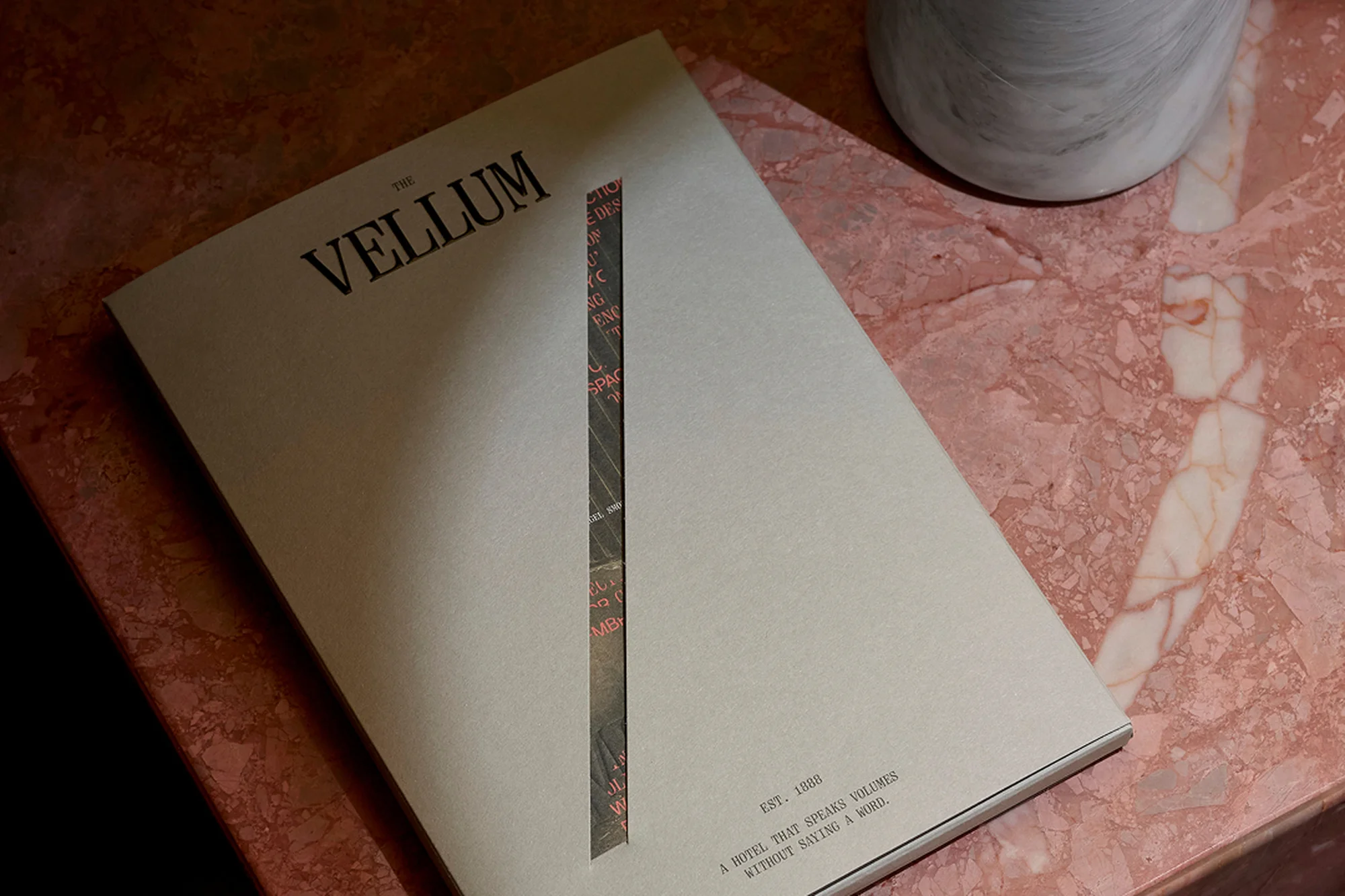 Close-up on a magazine cover titled 'The Vellum' sitting on a pink marble table next to a marble vase or object.