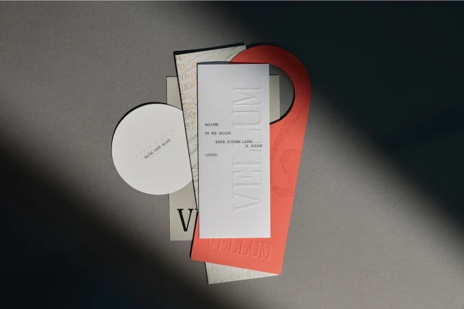 Arrangement of stationery items with a door hanger, cards, and paper circle against a grey background, captured with diffused light.