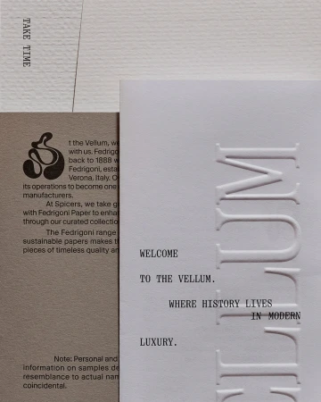 Close-up of paper samples featuring embossed and letterpress text on different paper textures and weights, with neutral tones.