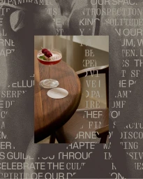 Cocktail glass with red drink and three raspberries on a wooden table beside a matching wooden chair.