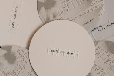 Close-up of overlapping round and curved white paper coasters featuring embossed typography and letterpress printing for Fedrigoni.