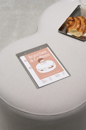 Overhead view of croissant and clipboard with a graphic of a person inside a sandwich sitting on an off-white padded surface.