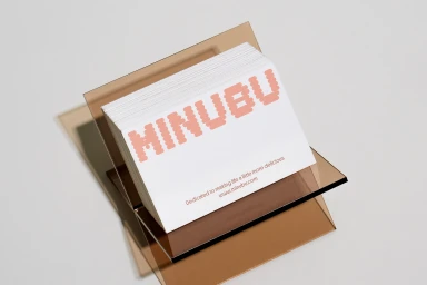 Stack of white business cards with pink branded typography resting in a transparent brown acrylic holder on a light surface.