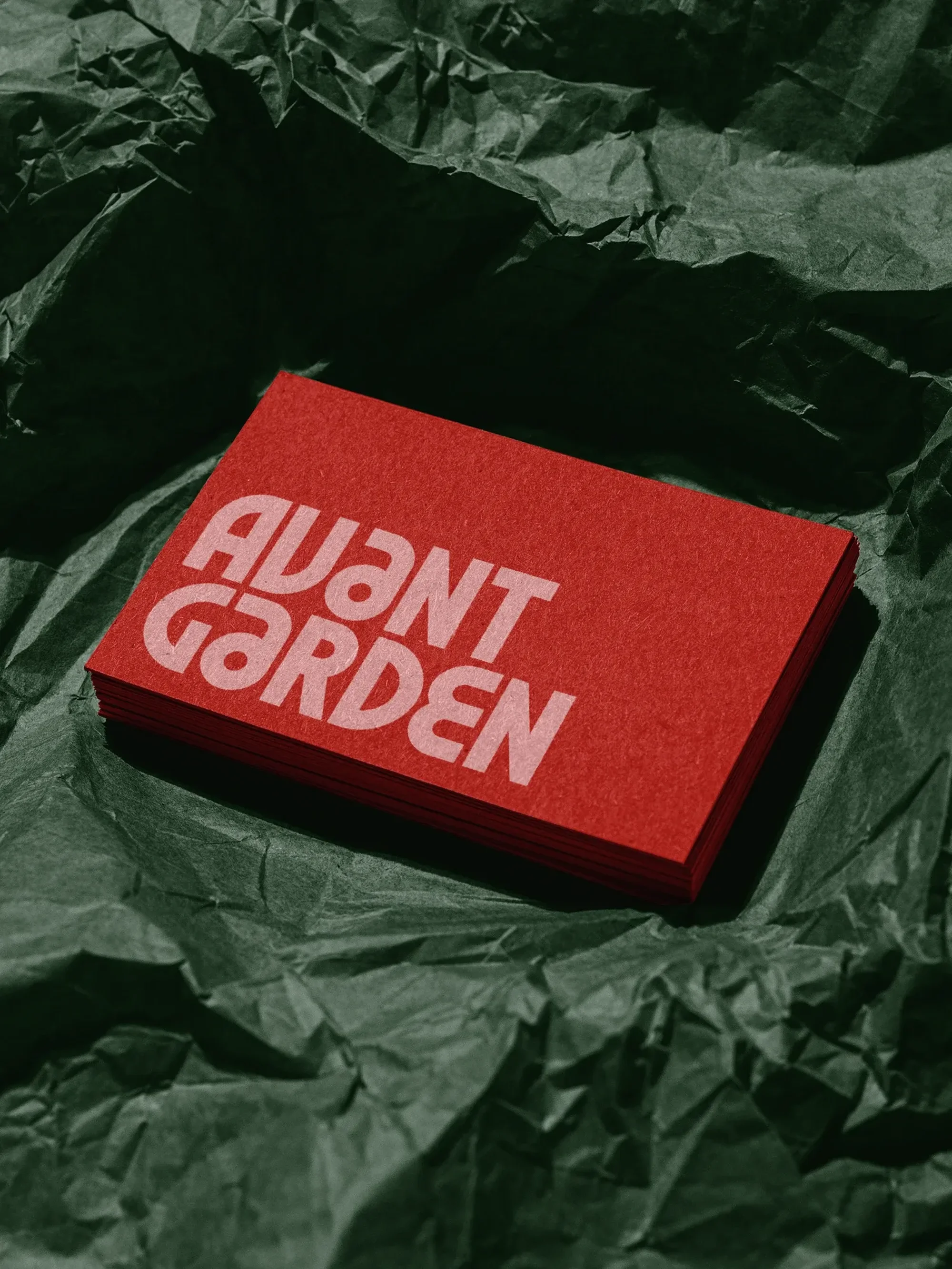 Stack of red business cards with white Avant Garden text on a crumpled dark green background, studio shot, top-down perspective.