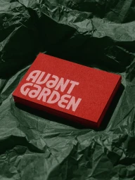 Red business card stack with Avant Garden typography resting on crumpled dark green paper