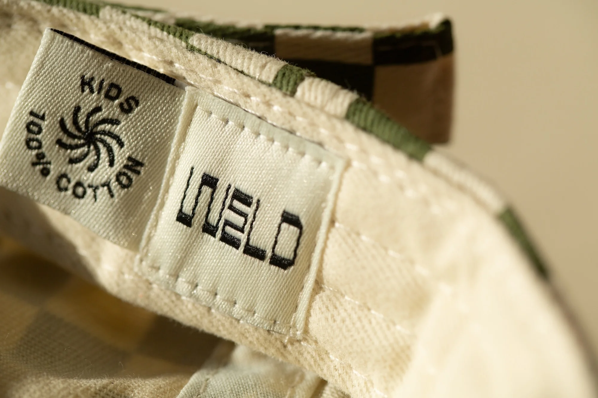 Close-up shot of a tag inside a checkered hat, highlighting the brand name 'Weld' and cotton material, conveying a sense of quality and craftsmanship.